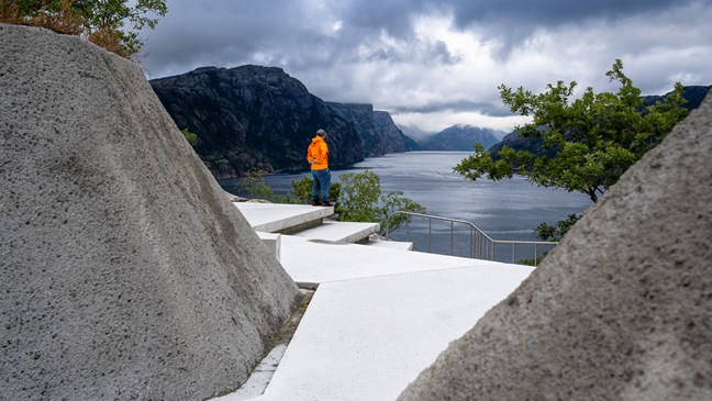 Betongsti går i en kløft av skråninger belagt med betong. Terrenget åpner seg opp med utsikt utover fjorden.