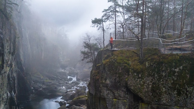 To menn og ei kvinne står og ser utover elv og juv fra et utsiktspunkt.