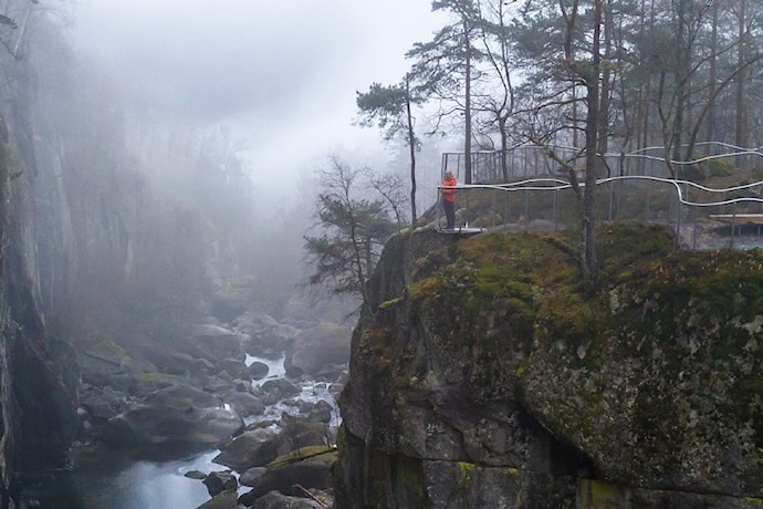 To menn og ei kvinne står og ser utover elv og juv fra et utsiktspunkt.