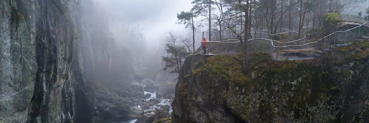 To menn og ei kvinne står og ser utover elv og juv fra et utsiktspunkt.