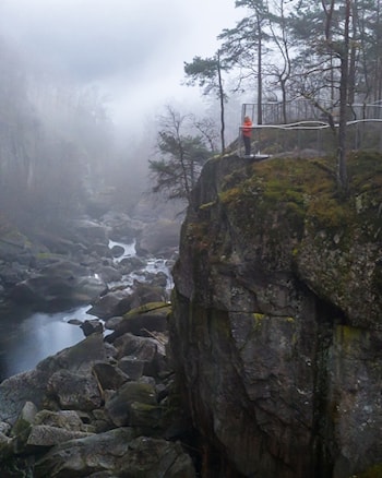 To menn og ei kvinne står og ser utover elv og juv fra et utsiktspunkt.