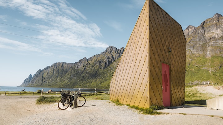 Toilet building by a beautiful sandy beach. The building is triangular and has a gold-plated exterior. 