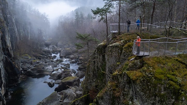 Mann står og ser utover elv og juv fra et utsiktspunkt.