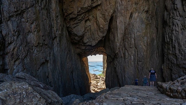 Steinsatt sti gjennom fjellåpningen i Torghatten. Hav og øyer er synlige gjennom åpningen.