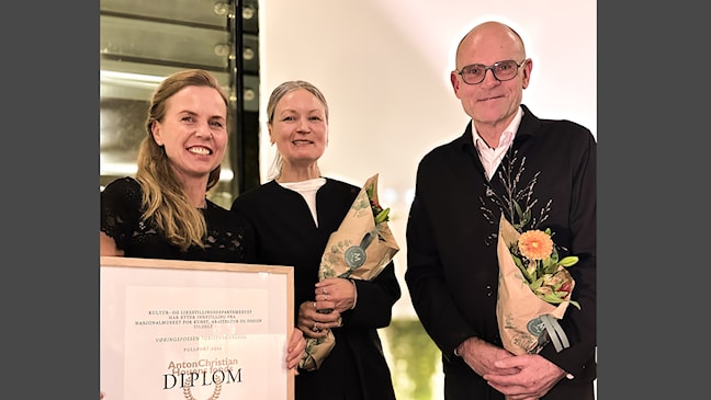 Tre personer med diplom og blomster under en prisutdeling for Vøringsfossen turistveganlegg.