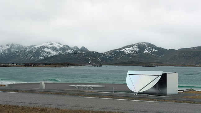 Et toalettbygg står ved en rund parkeringsplass. Hav og fjell i bakgrunnen.  hav og 