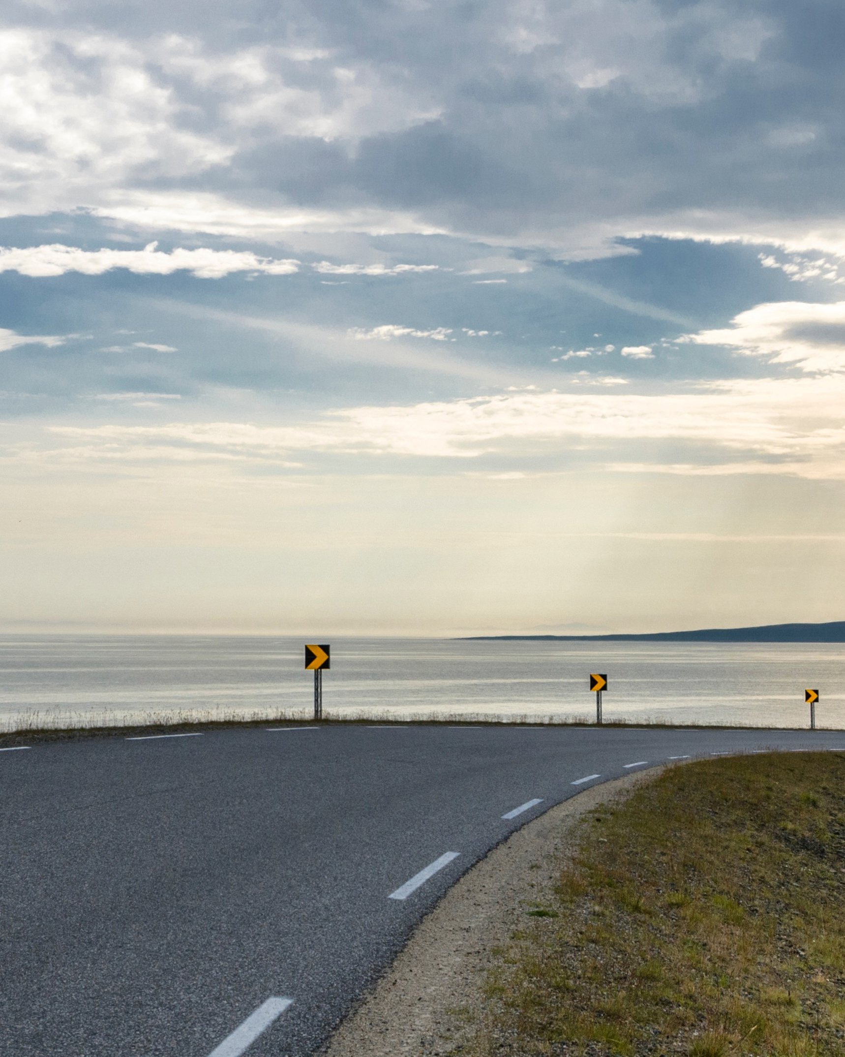The road out to sea on the horizonEuropean route 75 at Komagvær, with a wide view south towards the wide Varangerfjord.