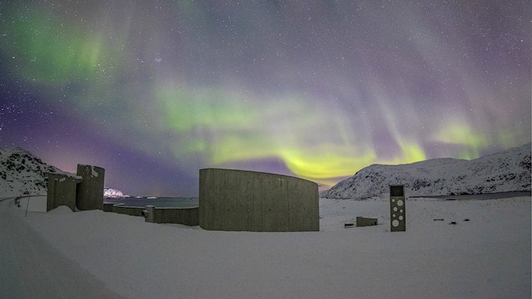 Northern lights over Selvika picnic area with a view of the sea and the road in the landscape
