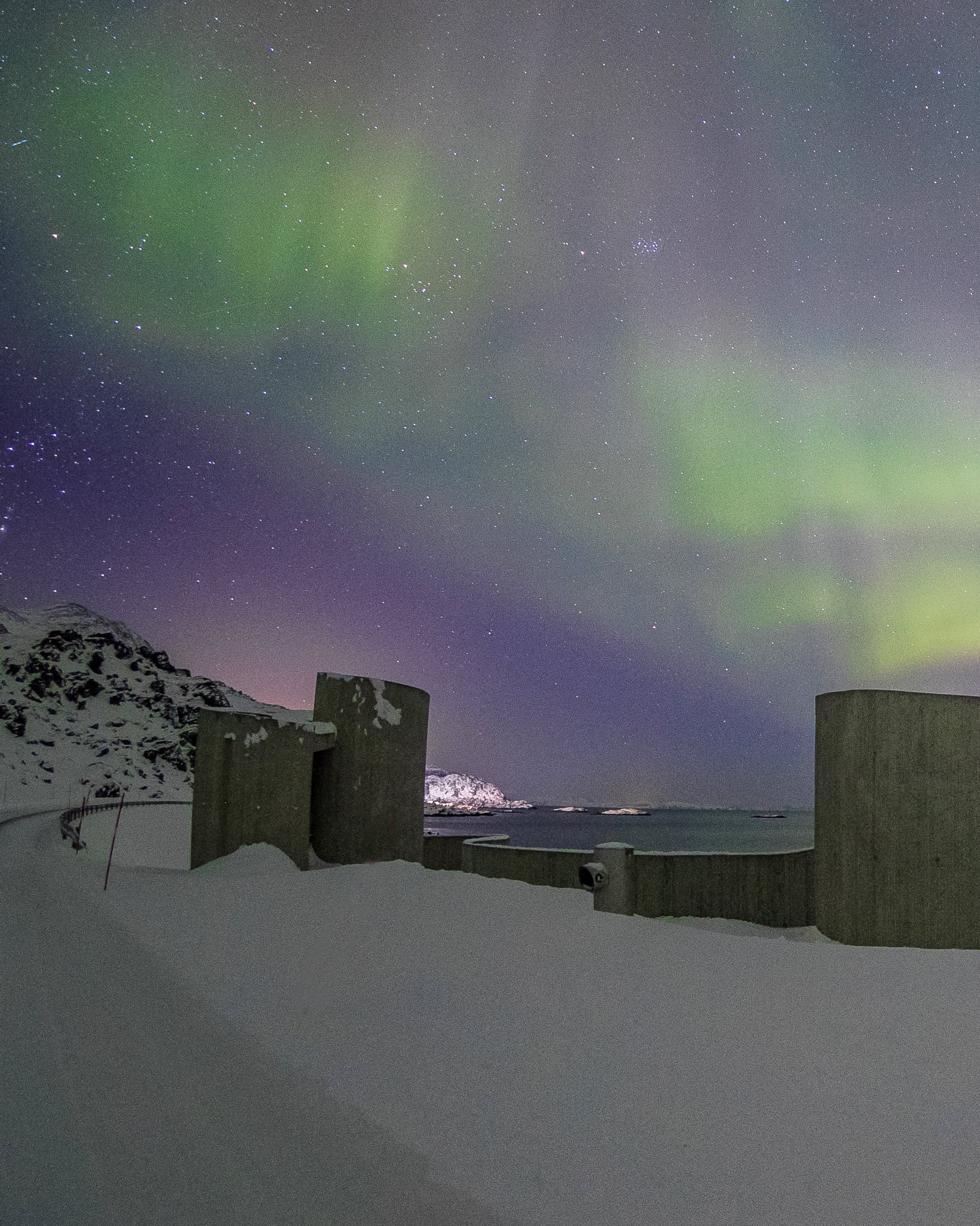 Northern lights over Selvika picnic area with a view of the sea and the road in the landscape