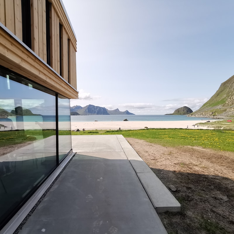 Section of wooden building with views of ocean, beach and mountains on the horizon.