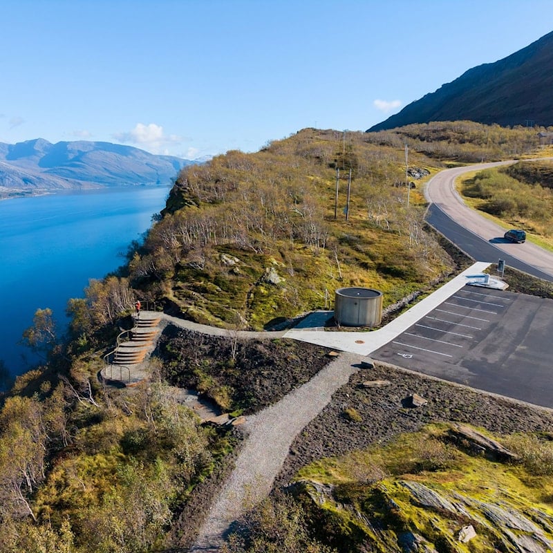 Oversiktsbilde av Sjonfjellet rasteplass med utsiktspunkt, toalettbygg og fjordlandskap.