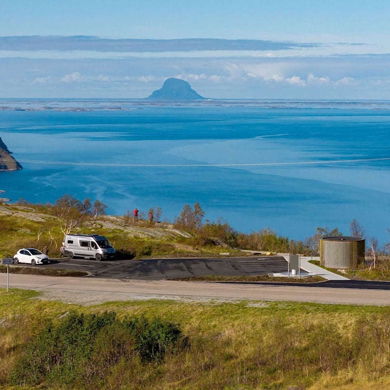 Person på parkeringsplass ser ut over fjord og fjell.