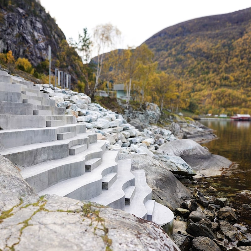 Betongtrapp ved kanten av Lærdalsfjorden. Trappa følgjer terrenget ned mot vatnet, med fjord, fjellside og grått skydekke i bakgrunnen.
