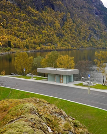 Moderne toalettbygg ved fjorden. Foran bygget er det gangareal og sitjeplassar, med bratte fjellsider og Lærdalsfjorden i bakgrunnen.