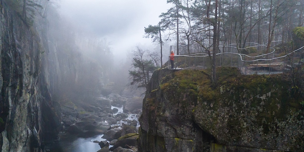 To menn og ei kvinne står og ser utover elv og juv fra et utsiktspunkt.